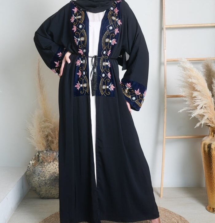 Stylish woman in embroidered black hijab abaya, standing in a chic indoor setting.